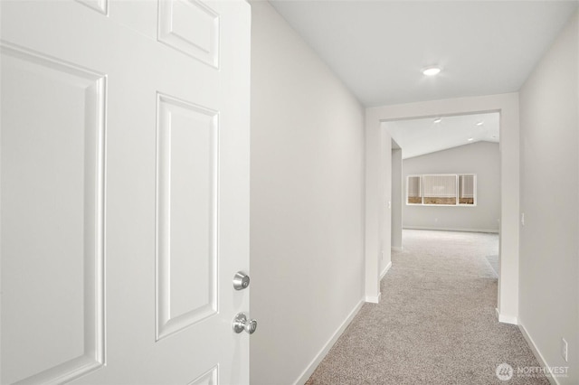 corridor featuring lofted ceiling, carpet, and baseboards