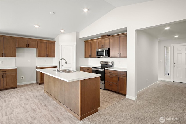 kitchen with lofted ceiling, a kitchen island with sink, stainless steel appliances, a sink, and light countertops