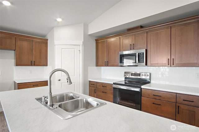 kitchen with a sink, light countertops, appliances with stainless steel finishes, backsplash, and brown cabinetry