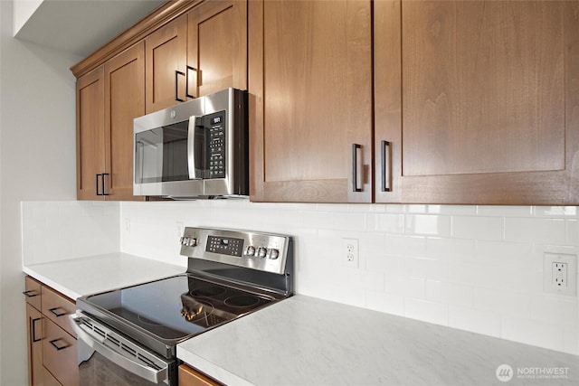 kitchen with stainless steel appliances, backsplash, light countertops, and brown cabinets