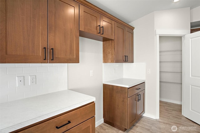 kitchen featuring backsplash, baseboards, brown cabinets, and light countertops