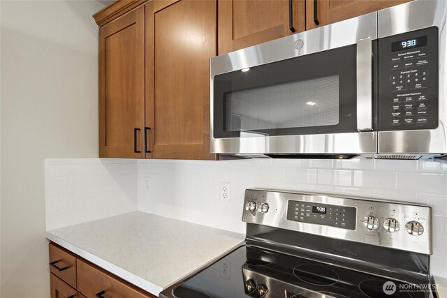 kitchen featuring light countertops, appliances with stainless steel finishes, brown cabinetry, and tasteful backsplash