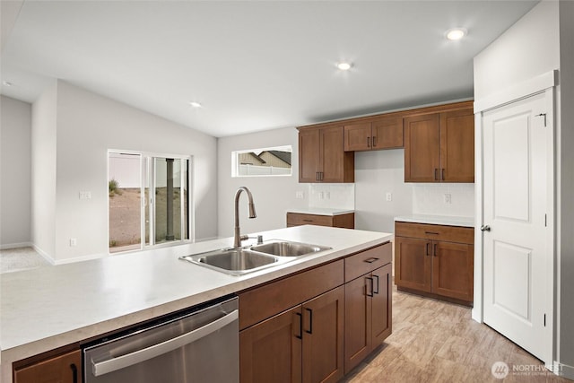 kitchen featuring lofted ceiling, a sink, light countertops, stainless steel dishwasher, and brown cabinetry