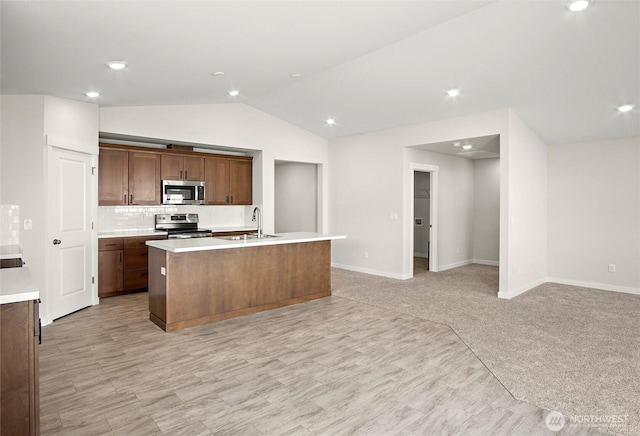 kitchen featuring a center island with sink, lofted ceiling, stainless steel appliances, light countertops, and a sink