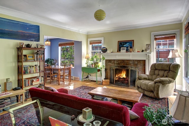 living room featuring baseboards, ornamental molding, a tiled fireplace, and wood finished floors