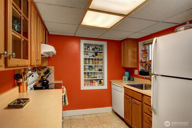 kitchen featuring under cabinet range hood, white appliances, a sink, light countertops, and brown cabinetry