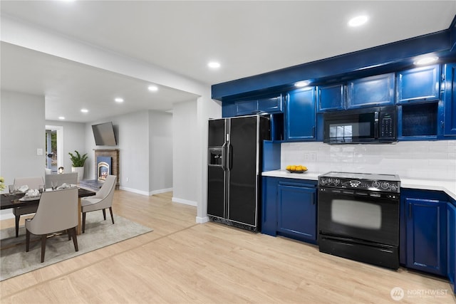 kitchen featuring blue cabinetry, black appliances, and a brick fireplace