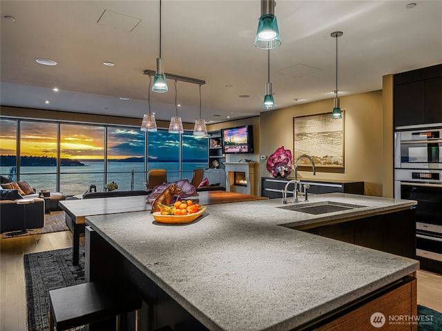 kitchen with light stone counters, a water view, hanging light fixtures, open floor plan, and a sink