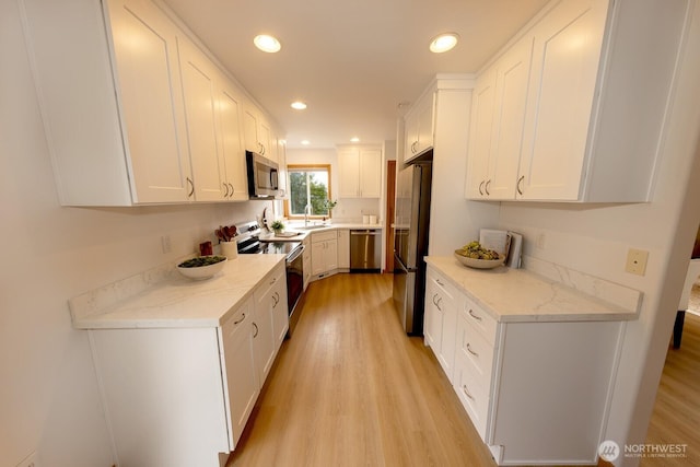 kitchen with light hardwood / wood-style flooring, stainless steel appliances, white cabinets, and light stone counters