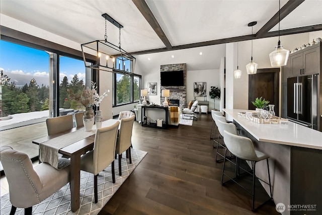 dining area featuring beamed ceiling, dark wood-type flooring, a notable chandelier, and a stone fireplace