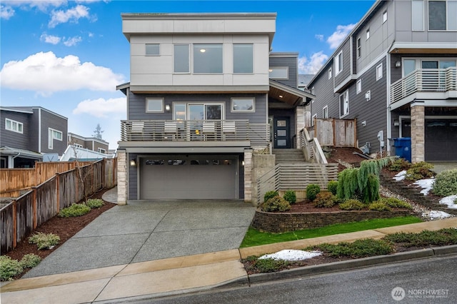 contemporary home featuring concrete driveway, a residential view, an attached garage, stairs, and fence