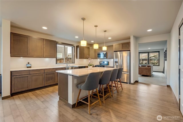 kitchen featuring stainless steel appliances, a sink, light countertops, a center island, and a kitchen bar