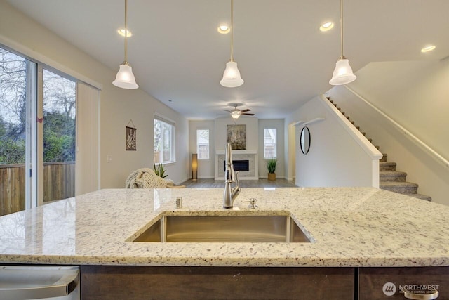 kitchen featuring a ceiling fan, light stone countertops, a fireplace, a sink, and open floor plan