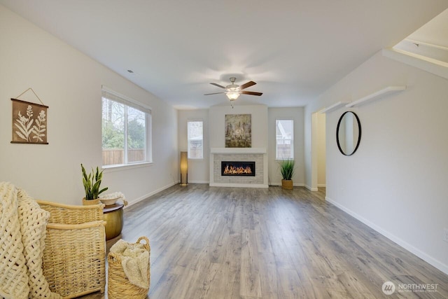 unfurnished living room featuring a glass covered fireplace, baseboards, a ceiling fan, and wood finished floors