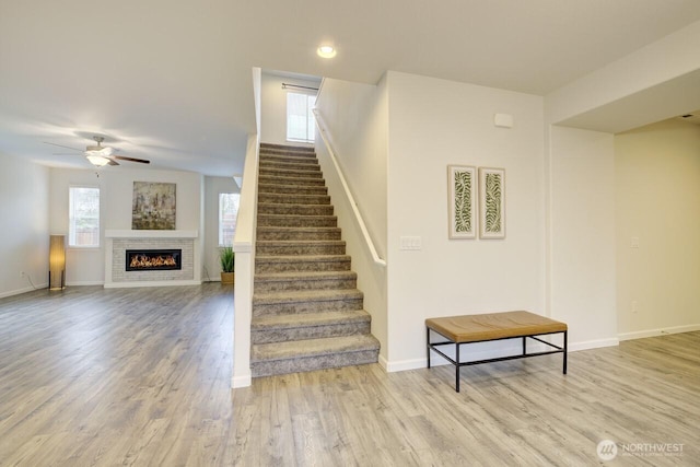 stairway with a glass covered fireplace, wood finished floors, baseboards, and a ceiling fan