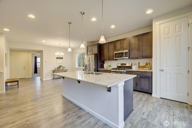 kitchen with light wood finished floors, dark brown cabinets, a breakfast bar, stainless steel appliances, and a sink