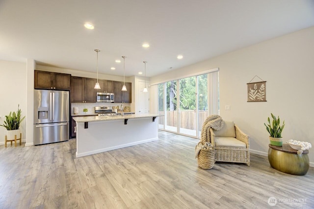 kitchen featuring light wood finished floors, dark brown cabinets, a breakfast bar, an island with sink, and appliances with stainless steel finishes