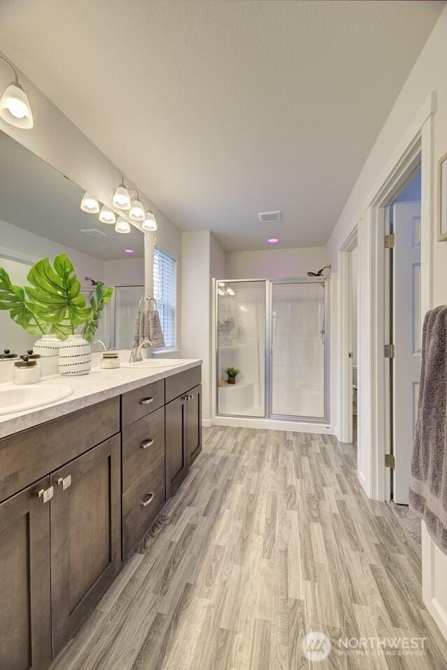 full bath with visible vents, a stall shower, wood finished floors, and double vanity