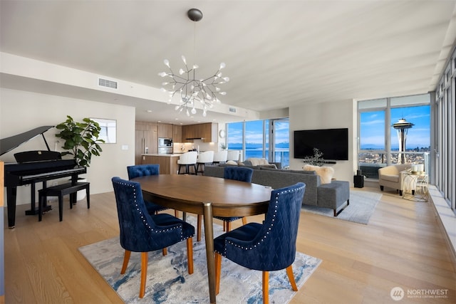 dining area with a chandelier, light wood finished floors, visible vents, and a healthy amount of sunlight