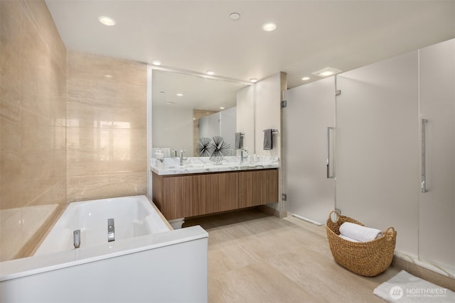 bathroom with double vanity, recessed lighting, a stall shower, a sink, and a bath