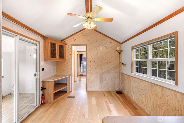 interior space featuring ornamental molding, light hardwood / wood-style flooring, vaulted ceiling, and wood walls