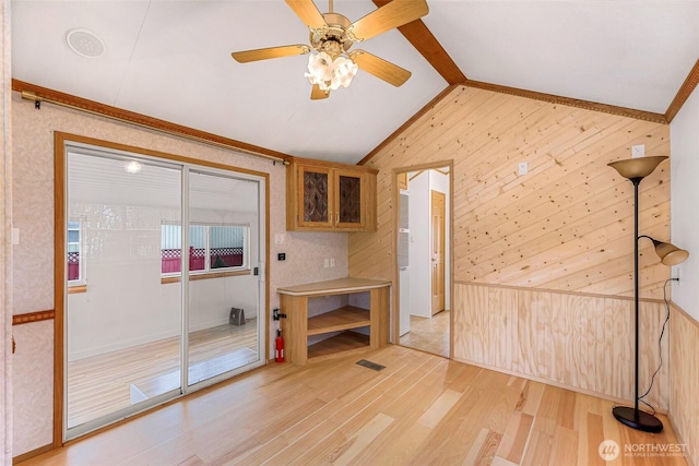 interior space with light hardwood / wood-style flooring, ceiling fan, lofted ceiling with beams, and wooden walls