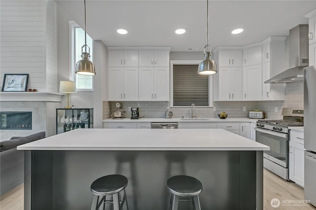 kitchen with stainless steel appliances, a sink, white cabinetry, light countertops, and wall chimney exhaust hood