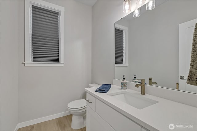 half bath featuring toilet, wood finished floors, vanity, and baseboards