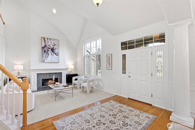 entrance foyer with decorative columns, stairs, light wood-type flooring, a fireplace, and high vaulted ceiling