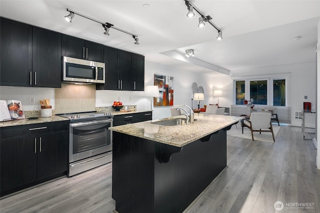 kitchen with a kitchen island with sink, light hardwood / wood-style flooring, sink, appliances with stainless steel finishes, and a kitchen bar