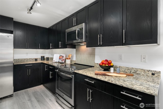 kitchen featuring appliances with stainless steel finishes, rail lighting, backsplash, light stone counters, and light hardwood / wood-style floors