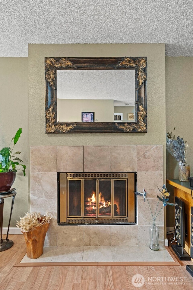 interior details featuring a textured ceiling, a tiled fireplace, wood finished floors, and baseboards