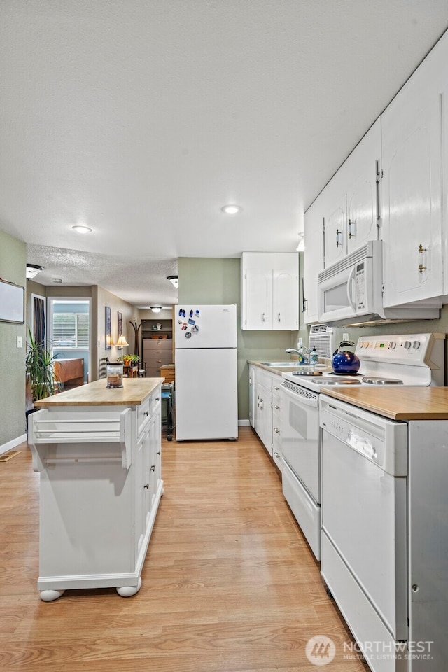 kitchen featuring white appliances, a center island, light wood-type flooring, white cabinetry, and wooden counters