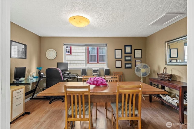 office area with a textured ceiling, light wood finished floors, and attic access