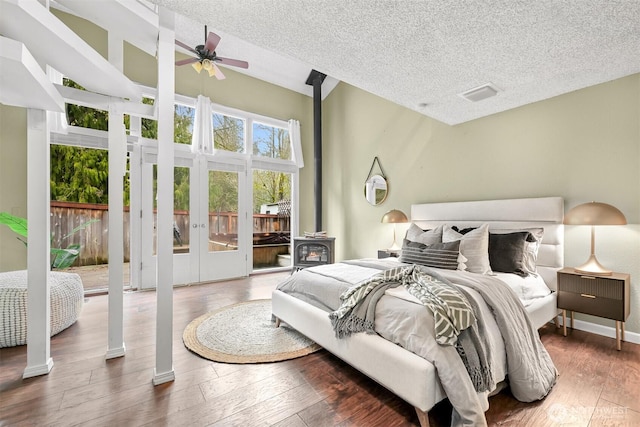 bedroom featuring french doors, a wood stove, access to exterior, a textured ceiling, and dark hardwood / wood-style floors