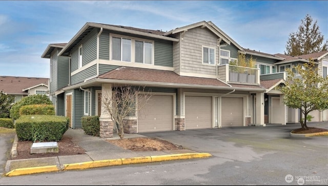 townhome / multi-family property featuring aphalt driveway, a shingled roof, an attached garage, a balcony, and stone siding