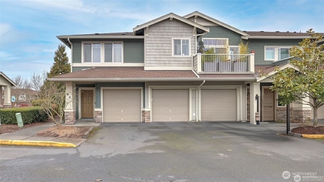 view of front of property with stone siding, driveway, a balcony, and an attached garage