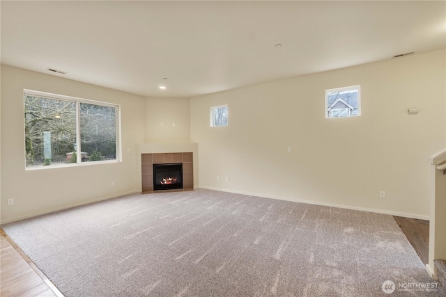 unfurnished living room featuring baseboards, plenty of natural light, and a tiled fireplace