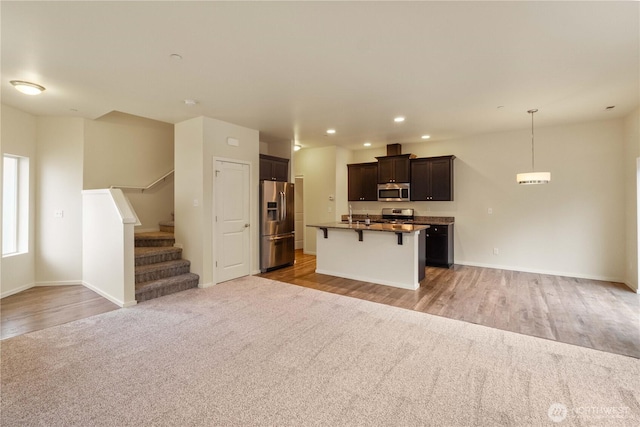 kitchen featuring dark countertops, appliances with stainless steel finishes, a center island with sink, a kitchen bar, and open floor plan