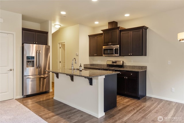 kitchen featuring a sink, dark brown cabinetry, an island with sink, stainless steel appliances, and a breakfast bar