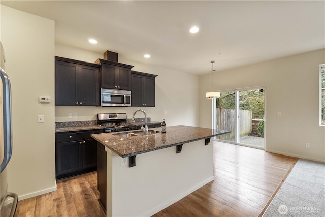 kitchen with a sink, pendant lighting, a kitchen bar, a kitchen island with sink, and stainless steel appliances