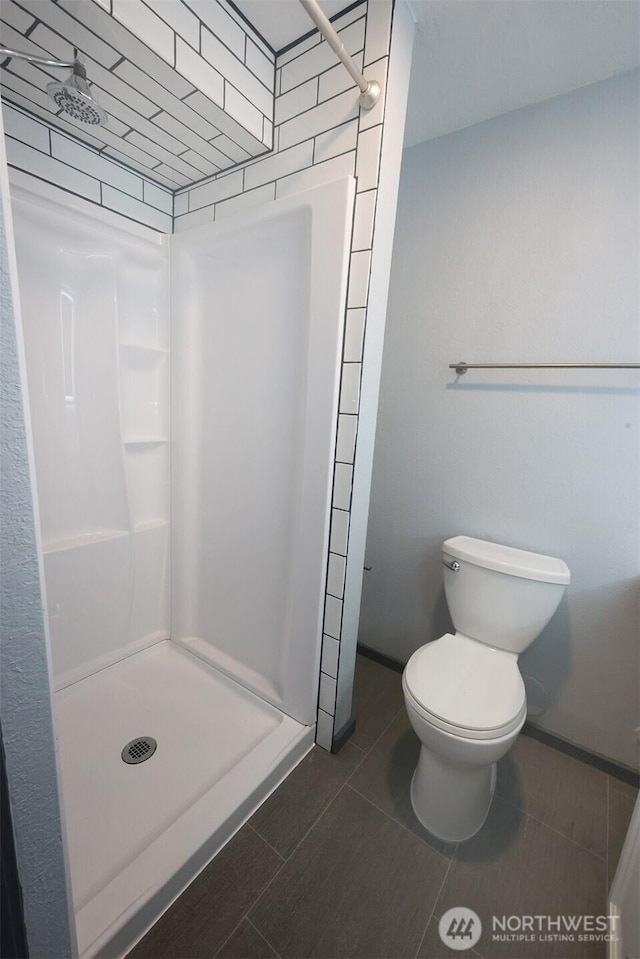 full bath featuring toilet, a shower stall, baseboards, and tile patterned flooring