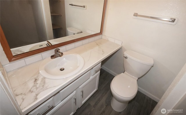 half bathroom with toilet, baseboards, wood finished floors, and vanity