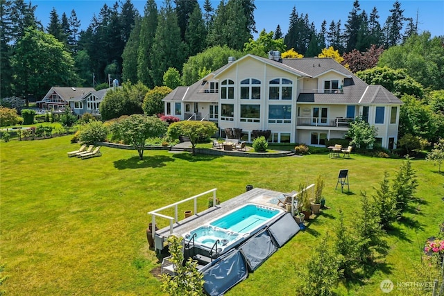 back of property featuring a patio, a balcony, a pool with connected hot tub, a yard, and a chimney