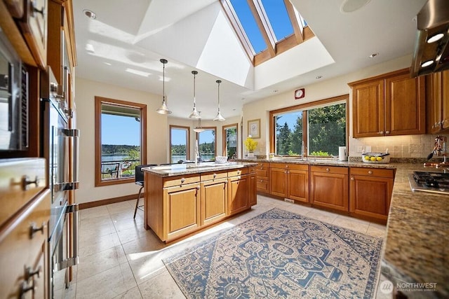 kitchen featuring vaulted ceiling with skylight, tasteful backsplash, hanging light fixtures, and brown cabinets