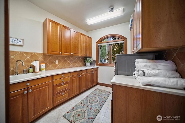 kitchen featuring brown cabinets, tasteful backsplash, light countertops, light tile patterned flooring, and a sink