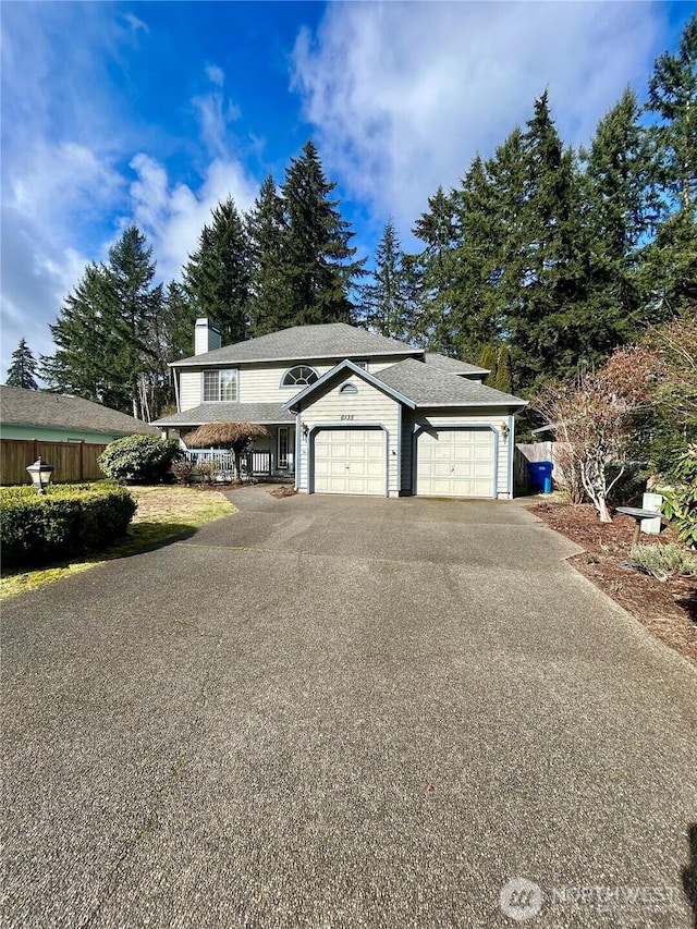 view of front facade featuring aphalt driveway, an attached garage, a chimney, and fence