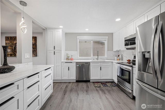 kitchen featuring appliances with stainless steel finishes, light wood-style floors, a sink, and backsplash