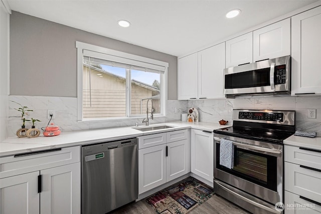 kitchen featuring stainless steel appliances, dark wood-style flooring, a sink, white cabinets, and decorative backsplash