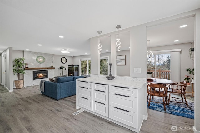 kitchen featuring light stone counters, decorative light fixtures, light wood-style floors, a fireplace, and white cabinetry